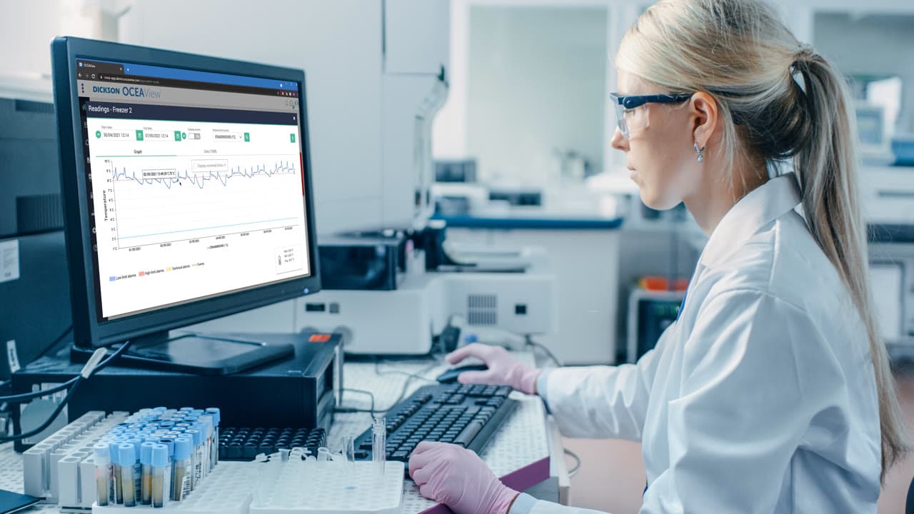 Lab technician using Dickson OCEAView monitoring dashboard to review temperature data in a pharmaceutical laboratory