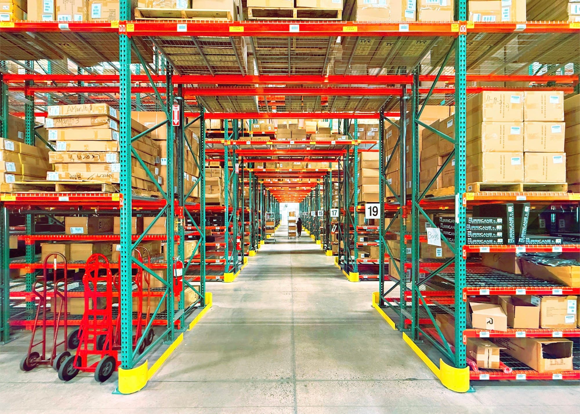 Workers walking through warehouse aisle with stocked shelves and pallets